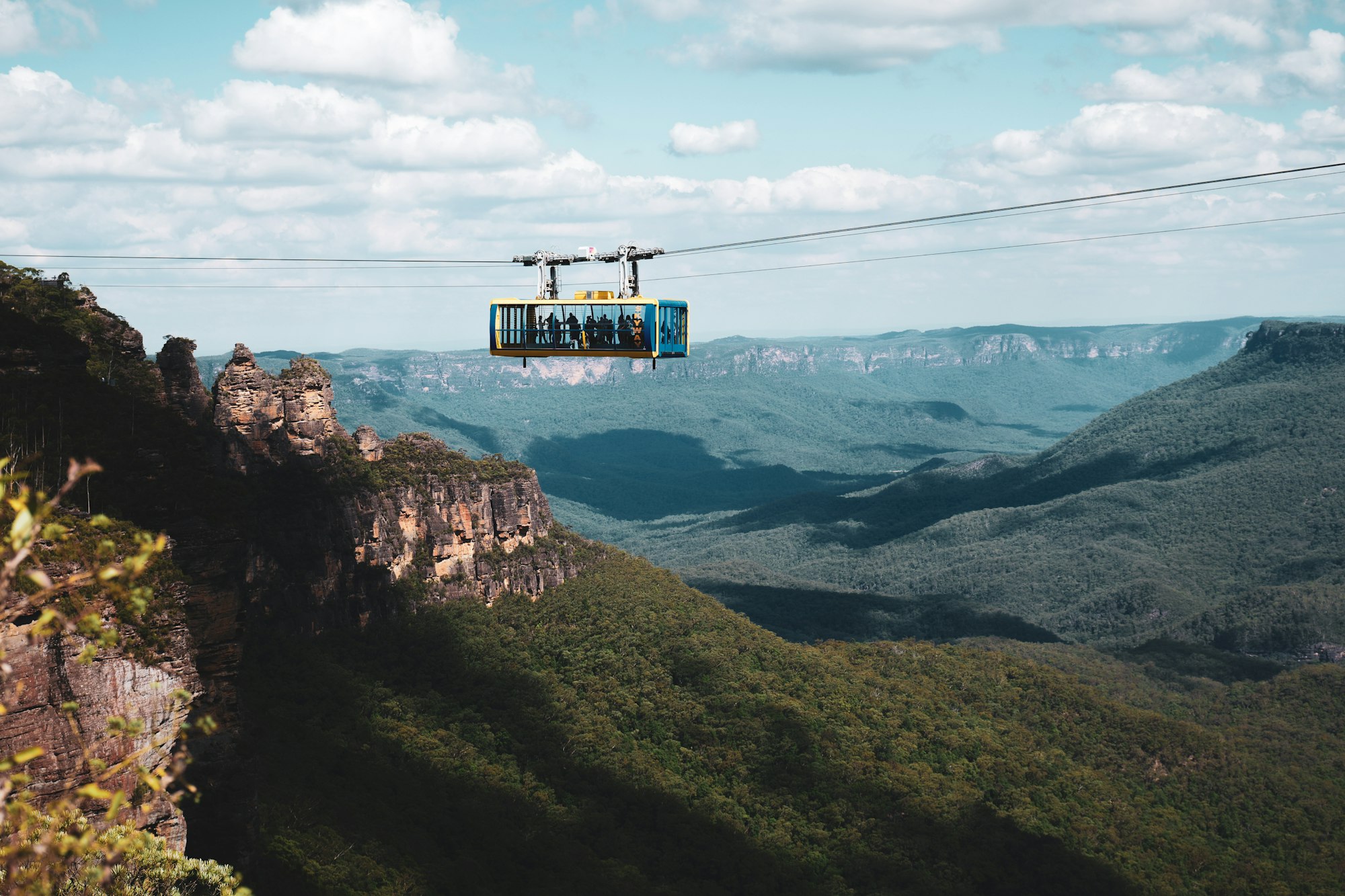 An aerial cableway car crossing a vast forested valley between sandstone cliffs